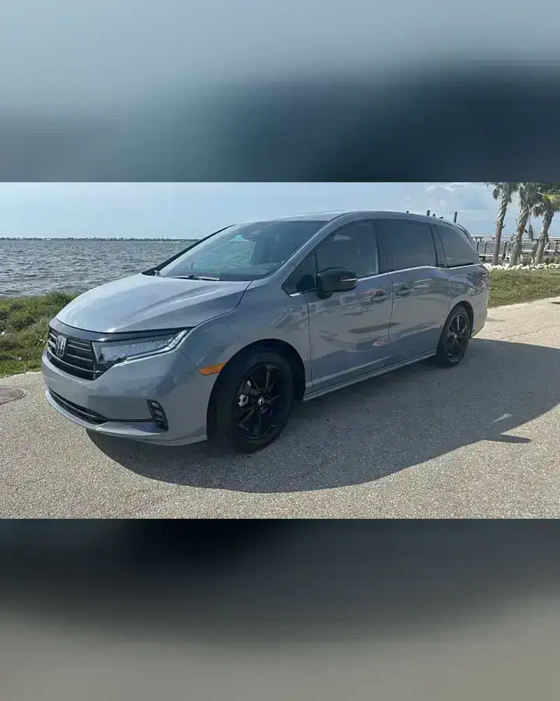 A 2024 Honda Odyssey from the SWFL Auto Rentals fleet, parked on a paved road beside the water