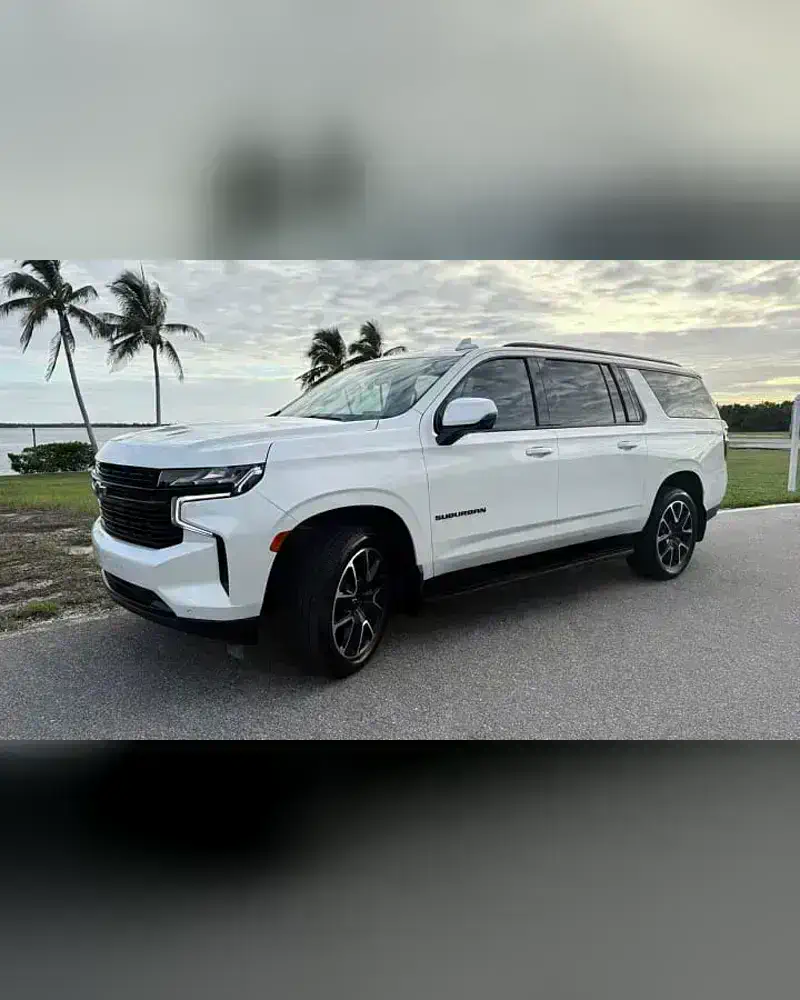 A 2023 Chevrolet Suburban from the SWFL Auto Rentals fleet, parked on a coastal road at sunset