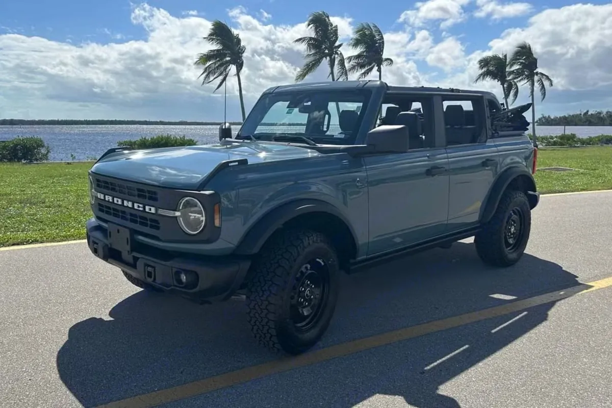 A blue-grey Ford Bronco from the SWFL Auto Rentals fleet parked on a palm-lined waterfront road in Southwest Florida